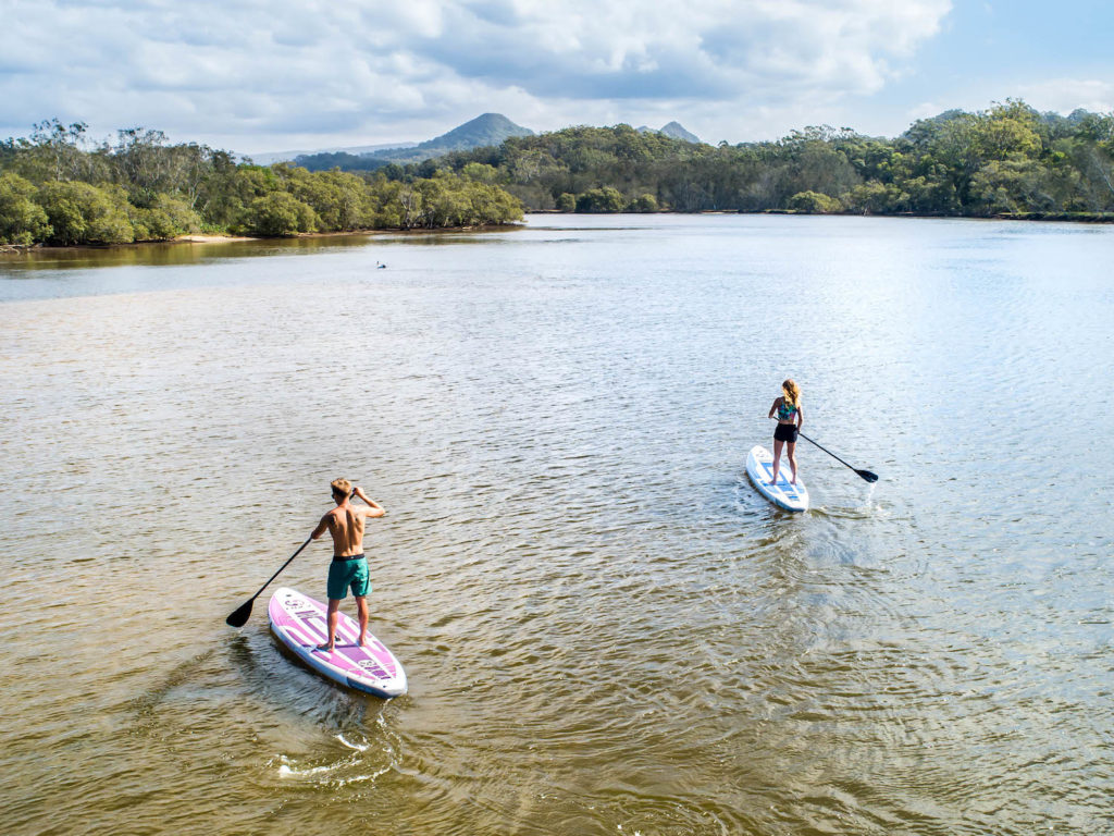 Two Nixy SUPs paddle in river